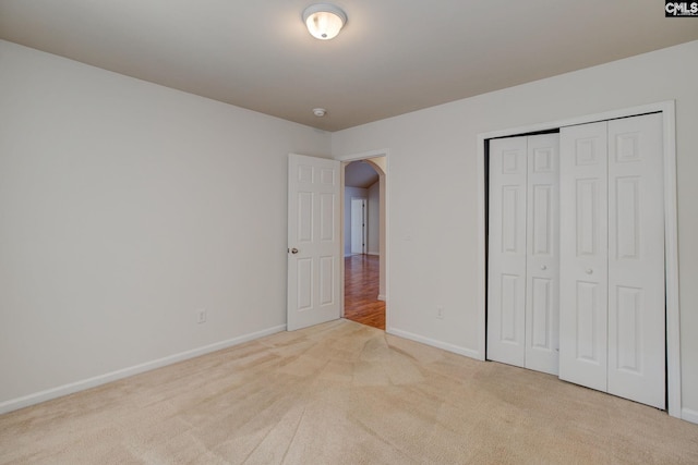 unfurnished bedroom with arched walkways, carpet flooring, a closet, and baseboards