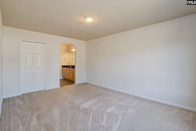 unfurnished bedroom featuring connected bathroom, baseboards, a closet, light carpet, and arched walkways