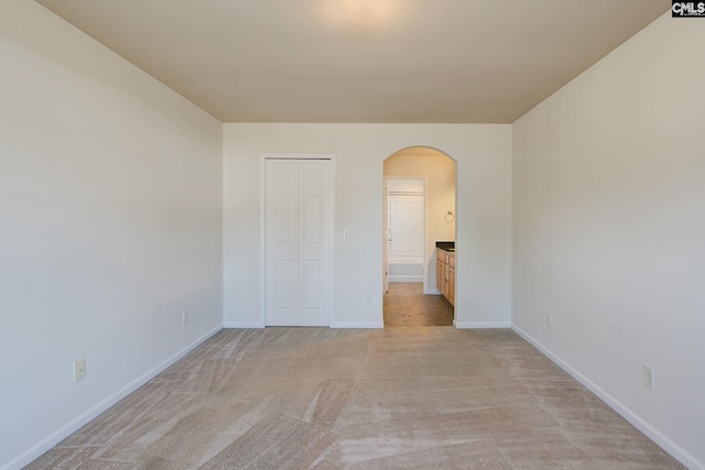 unfurnished bedroom featuring light carpet, connected bathroom, arched walkways, a closet, and baseboards