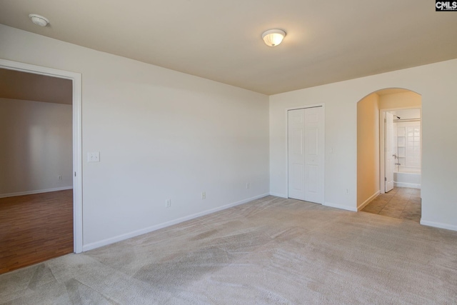 unfurnished bedroom featuring ensuite bath, carpet, arched walkways, and baseboards