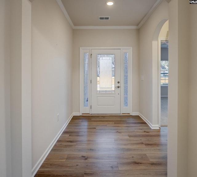 foyer entrance with wood finished floors, baseboards, visible vents, arched walkways, and ornamental molding