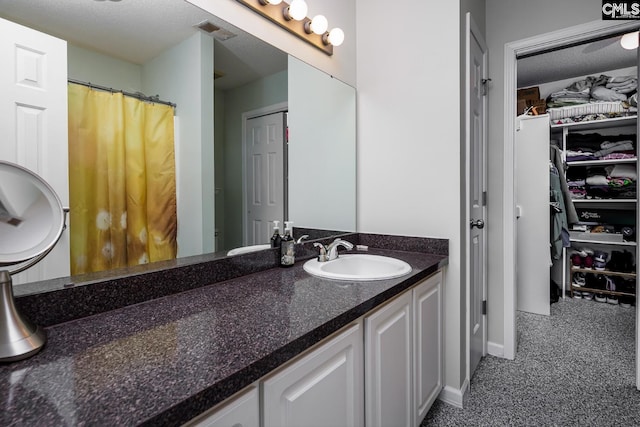 bathroom featuring visible vents, a textured ceiling, vanity, and a walk in closet