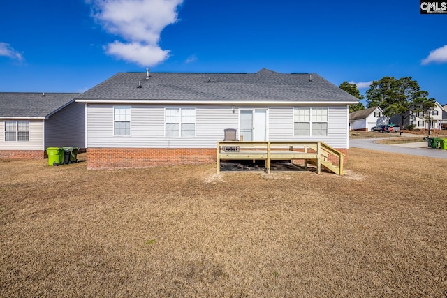 rear view of property with a wooden deck, a yard, and roof with shingles