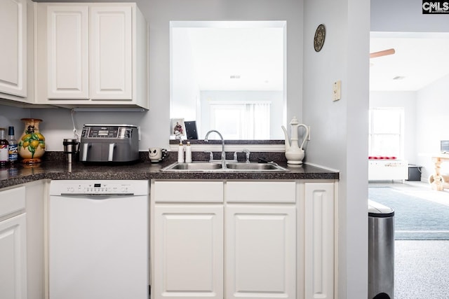 kitchen with dark countertops, a sink, white cabinets, and white dishwasher