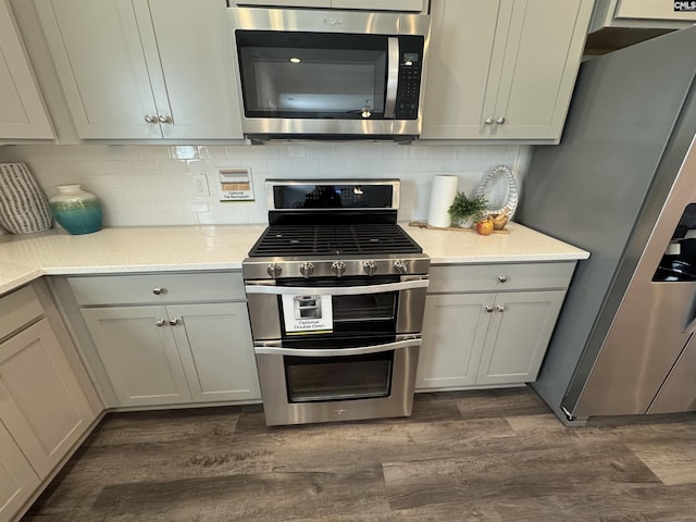 kitchen featuring tasteful backsplash, appliances with stainless steel finishes, light stone counters, and dark wood-style flooring