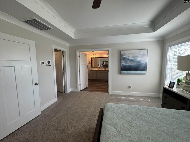 carpeted bedroom with a raised ceiling, baseboards, visible vents, and ornamental molding