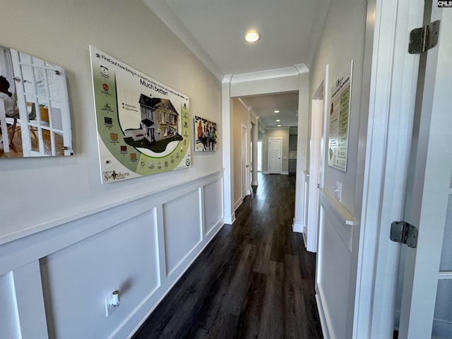 corridor with dark wood-type flooring, recessed lighting, a decorative wall, wainscoting, and crown molding