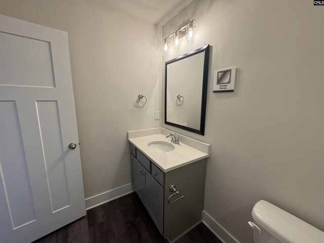 half bathroom with vanity, toilet, wood finished floors, and baseboards