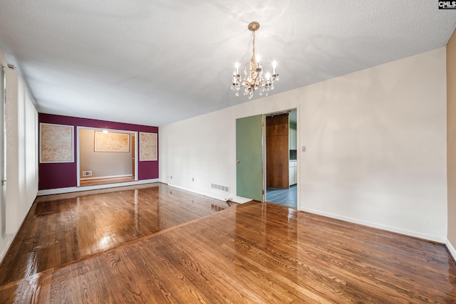 spare room featuring visible vents, a notable chandelier, a textured ceiling, wood finished floors, and baseboards