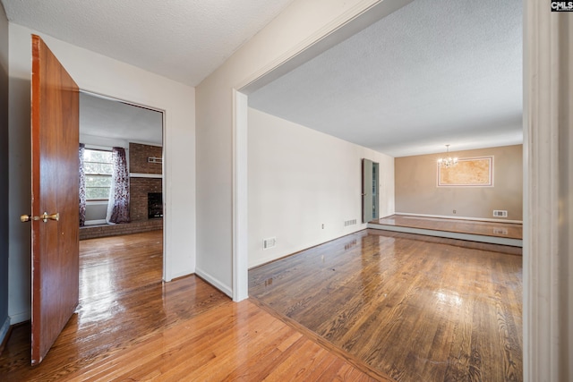 unfurnished room with light wood finished floors, visible vents, a fireplace, a notable chandelier, and a textured ceiling