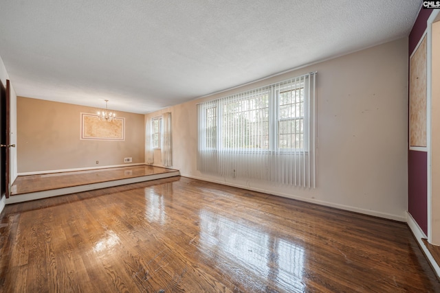 unfurnished room featuring an inviting chandelier, wood finished floors, baseboards, and a textured ceiling