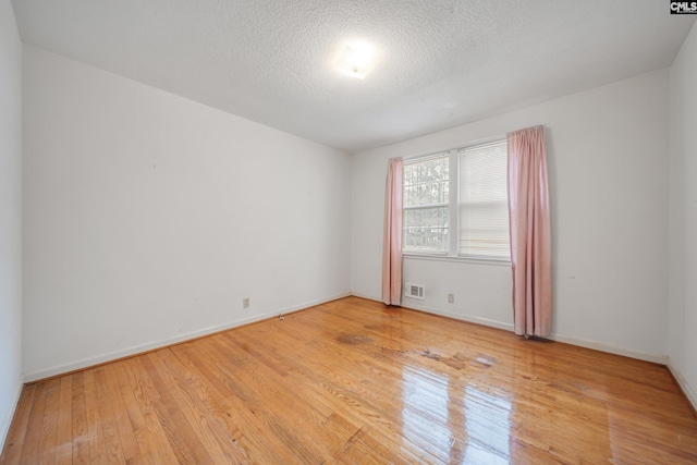 unfurnished room with a textured ceiling, baseboards, visible vents, and light wood-type flooring