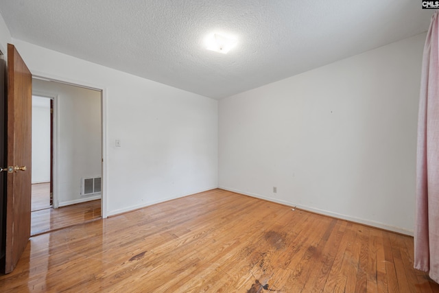 unfurnished room featuring light wood-style flooring, baseboards, visible vents, and a textured ceiling