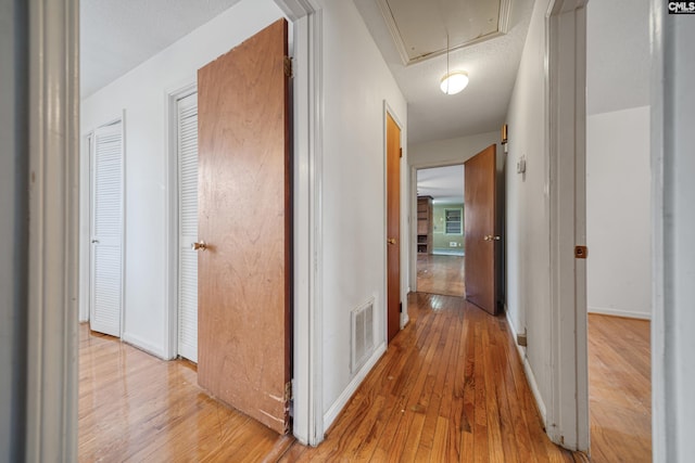 corridor with a textured ceiling, attic access, visible vents, and light wood-type flooring