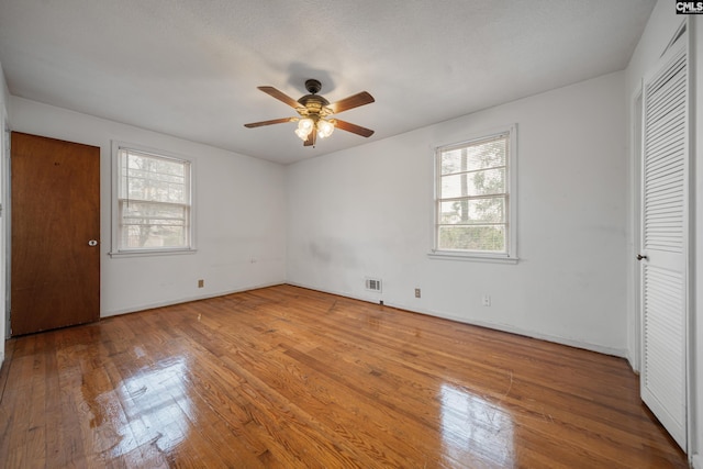 unfurnished bedroom with visible vents, multiple windows, a ceiling fan, and wood-type flooring