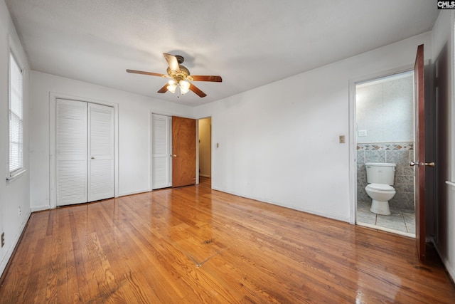 unfurnished bedroom with light wood-type flooring, multiple closets, connected bathroom, and a ceiling fan