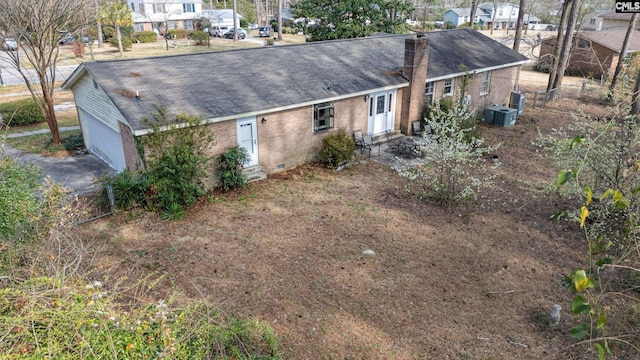 view of home's exterior with entry steps, a shingled roof, a garage, brick siding, and central AC unit