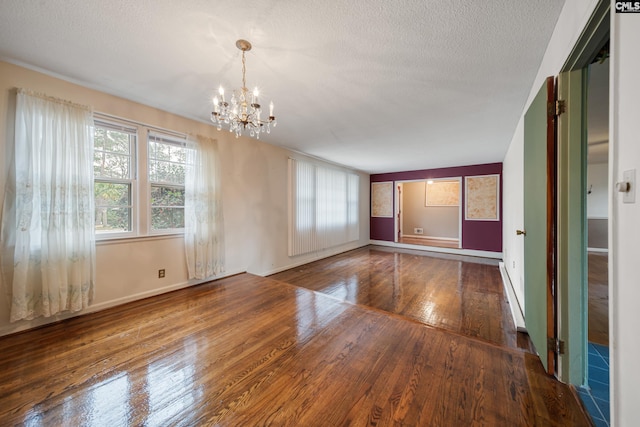 unfurnished room with baseboards, a textured ceiling, an inviting chandelier, and hardwood / wood-style flooring