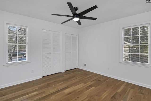 unfurnished bedroom featuring baseboards, multiple closets, a ceiling fan, and dark wood-style flooring