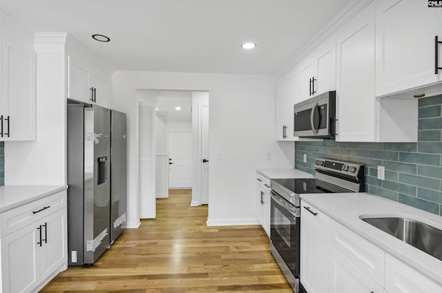 kitchen with backsplash, light countertops, light wood-style flooring, white cabinets, and stainless steel appliances