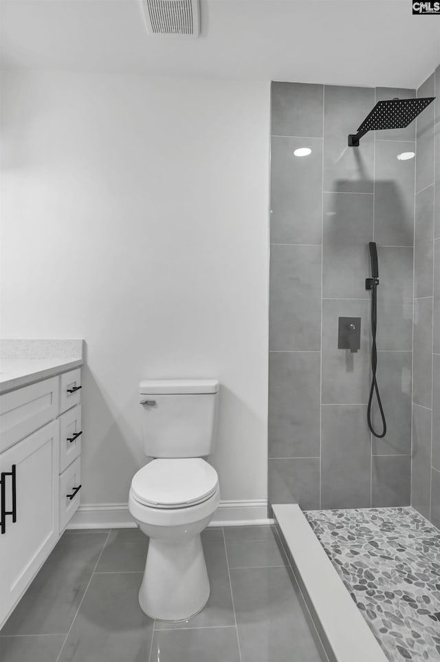 bathroom featuring visible vents, baseboards, toilet, a tile shower, and vanity