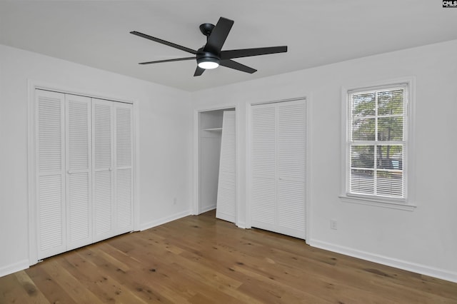 unfurnished bedroom with two closets, baseboards, and wood finished floors