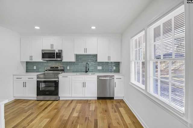 kitchen with light wood-type flooring, stainless steel appliances, light countertops, and a sink