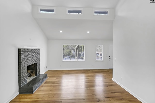 unfurnished living room with a brick fireplace, baseboards, recessed lighting, a high ceiling, and wood finished floors