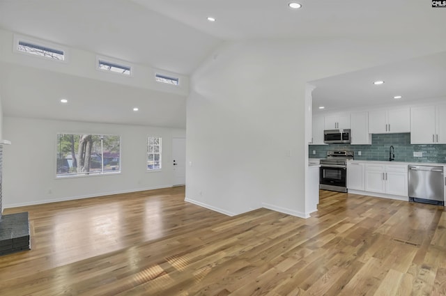 unfurnished living room featuring baseboards, recessed lighting, light wood-style flooring, high vaulted ceiling, and a sink