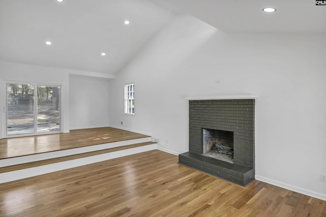 unfurnished living room with a healthy amount of sunlight, a brick fireplace, high vaulted ceiling, and wood finished floors