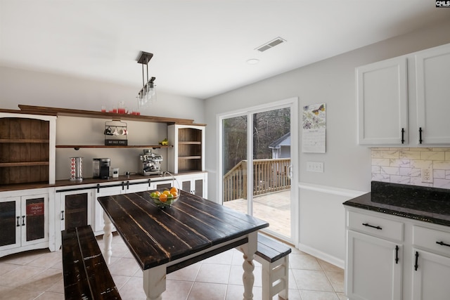 kitchen featuring visible vents, white cabinetry, dark stone counters, light tile patterned flooring, and decorative backsplash