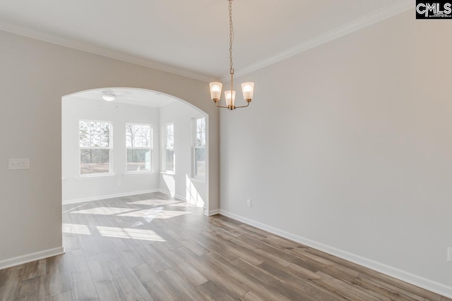 spare room with baseboards, arched walkways, wood finished floors, and crown molding