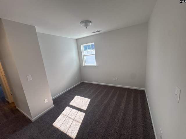 spare room featuring visible vents, baseboards, and dark colored carpet