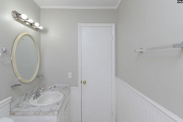 half bathroom with vanity, crown molding, toilet, and wainscoting