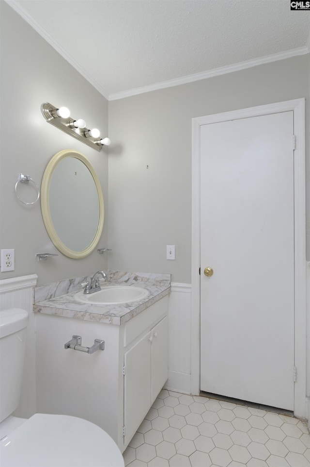 bathroom featuring vanity, a wainscoted wall, ornamental molding, a textured ceiling, and toilet