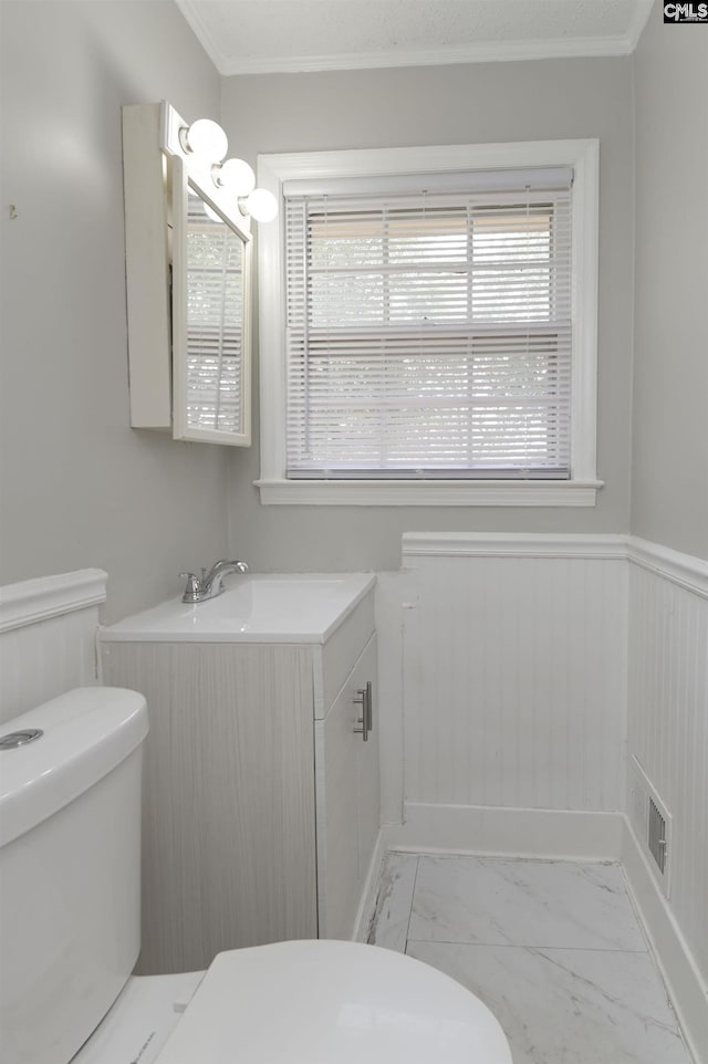 bathroom featuring ornamental molding, toilet, marble finish floor, and wainscoting