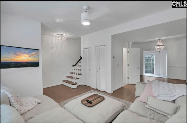 living room featuring stairs, a notable chandelier, wood finished floors, and baseboards