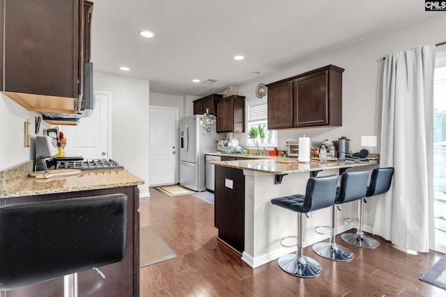 kitchen featuring light stone countertops, dark brown cabinetry, stainless steel fridge with ice dispenser, a peninsula, and wood finished floors