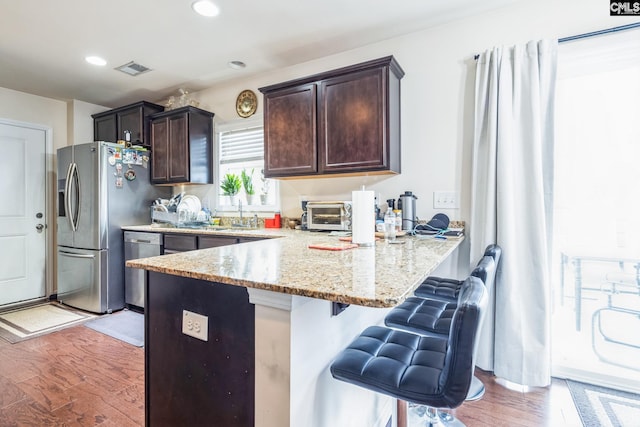 kitchen with a peninsula, a breakfast bar area, appliances with stainless steel finishes, and light wood finished floors