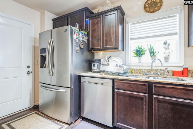 kitchen featuring a sink, light stone counters, dark brown cabinetry, and appliances with stainless steel finishes