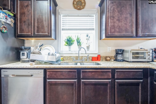 kitchen with a sink, dark brown cabinets, light stone countertops, and stainless steel dishwasher