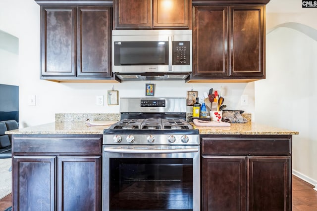 kitchen featuring dark brown cabinetry, light stone countertops, baseboards, and appliances with stainless steel finishes