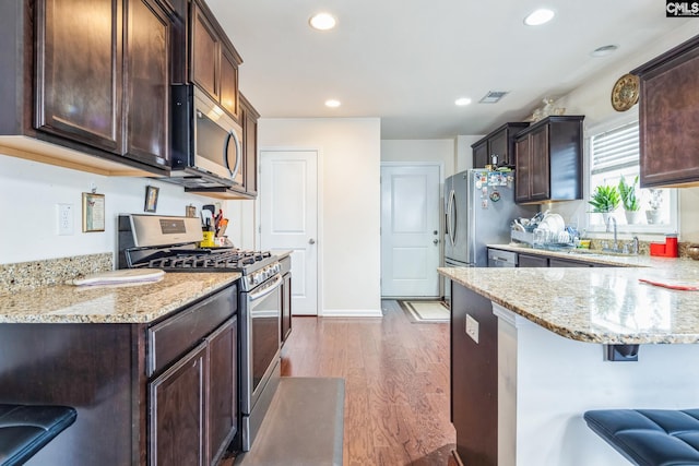 kitchen with a sink, dark brown cabinetry, light wood-style floors, appliances with stainless steel finishes, and a kitchen breakfast bar