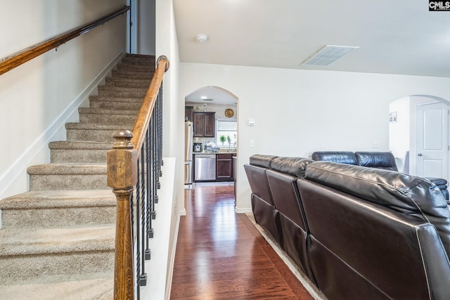 stairway with arched walkways, visible vents, baseboards, and wood finished floors