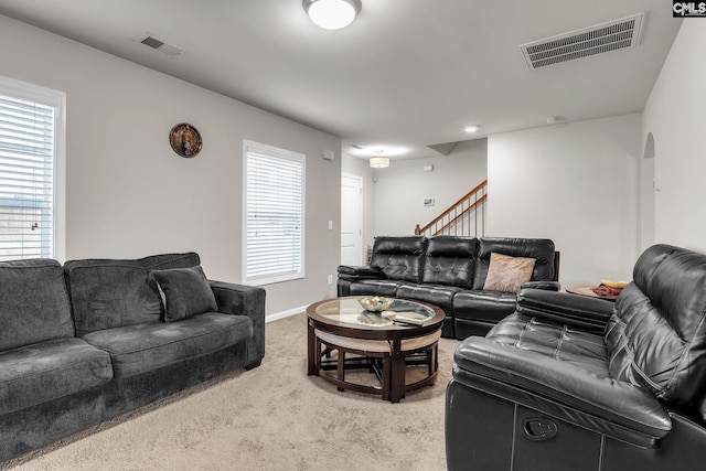 living room featuring stairs, light colored carpet, visible vents, and arched walkways