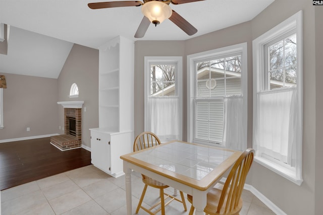 dining space featuring light tile patterned floors, a fireplace, baseboards, and ceiling fan