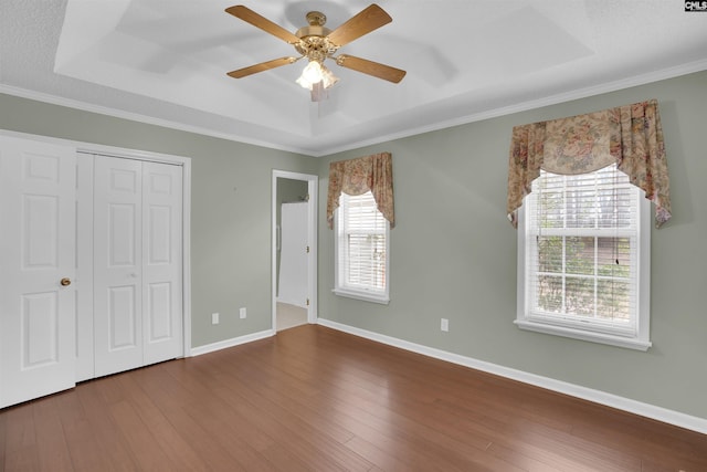 unfurnished bedroom featuring crown molding, baseboards, a tray ceiling, hardwood / wood-style floors, and a closet