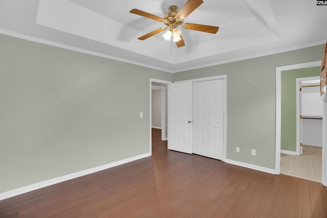 unfurnished bedroom featuring a tray ceiling, dark wood-style floors, a closet, crown molding, and baseboards