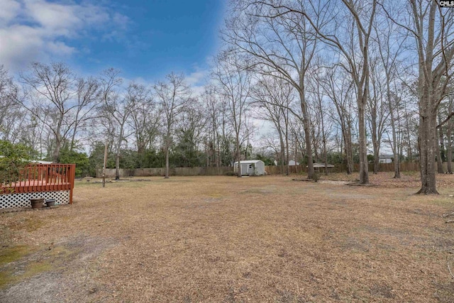 view of yard with an outbuilding, a wooden deck, a storage shed, and fence