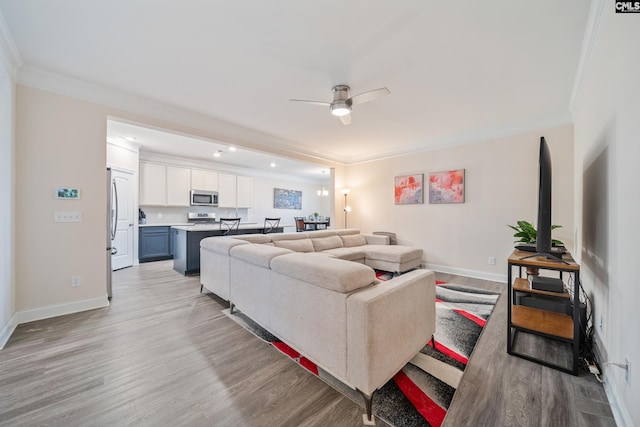 living area with ornamental molding, light wood-style floors, baseboards, and ceiling fan